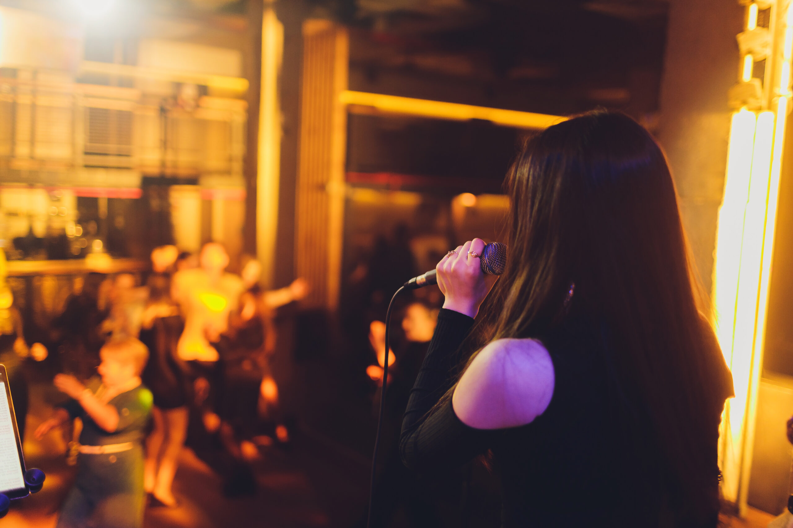 Beautiful Singing Girl. Beauty Glamor fashion Woman with Microphone over Blinking bokeh night background. Glamour Model Singer. Karaoke song. Karaoke party.
